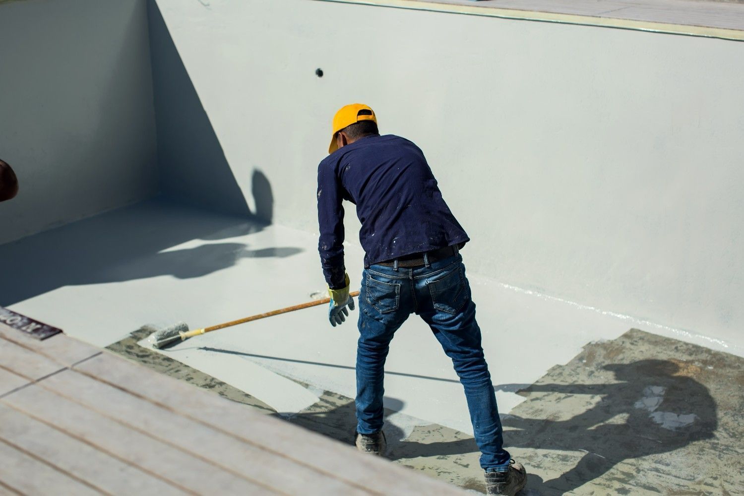 Person Painting a Pool's Interior With a Roller. the Pool is Empty and Gray, With the Worker Wearing a Yellow Hat and Jeans — Campbell Built in Newcastle, NSW