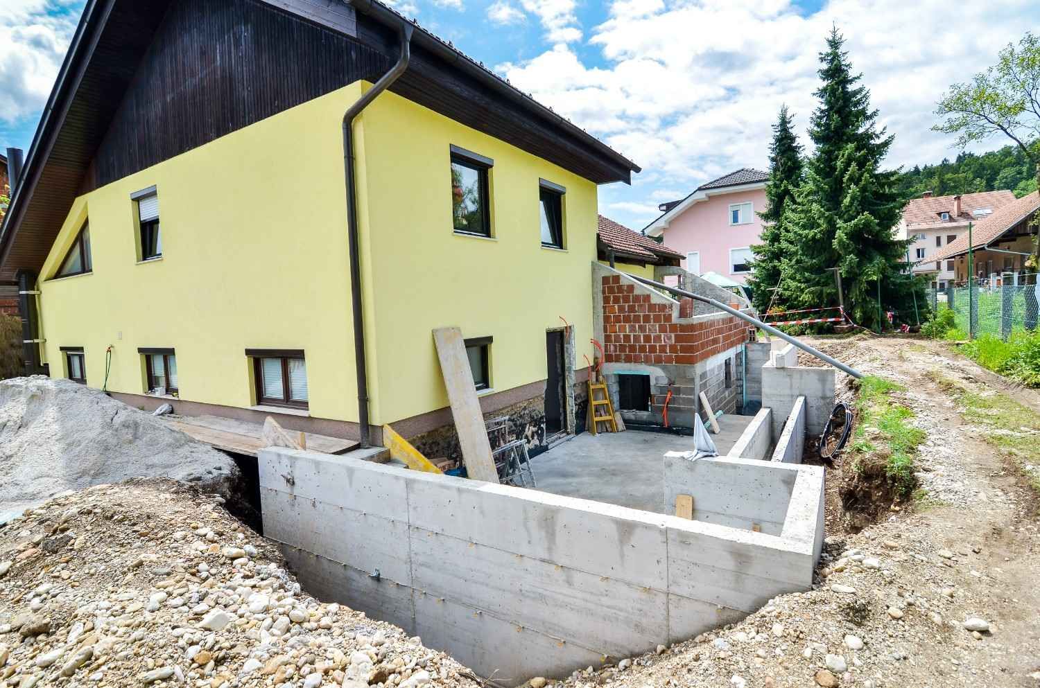A Yellow Two-story House With a Basement Under Construction. Cement Walls and Dirt Surround the Building — Campbell Built in Nelson Bay, NSW