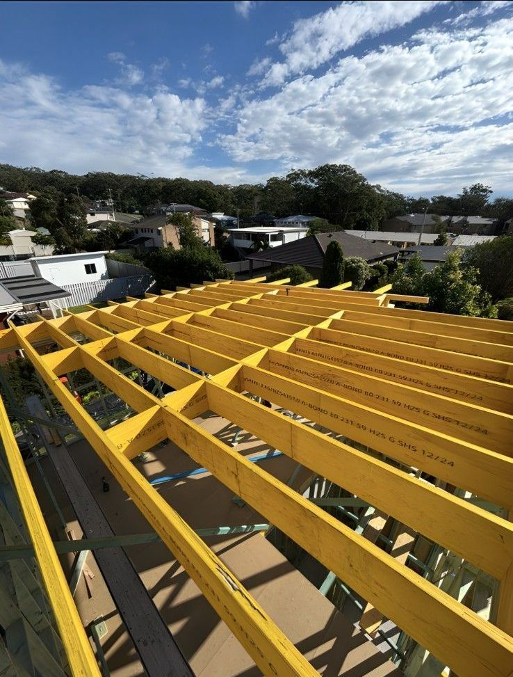 View of a Roof Under Construction, Showing Yellow Wooden Beams and the Sky — Campbell Built in Nelson Bay, NSW