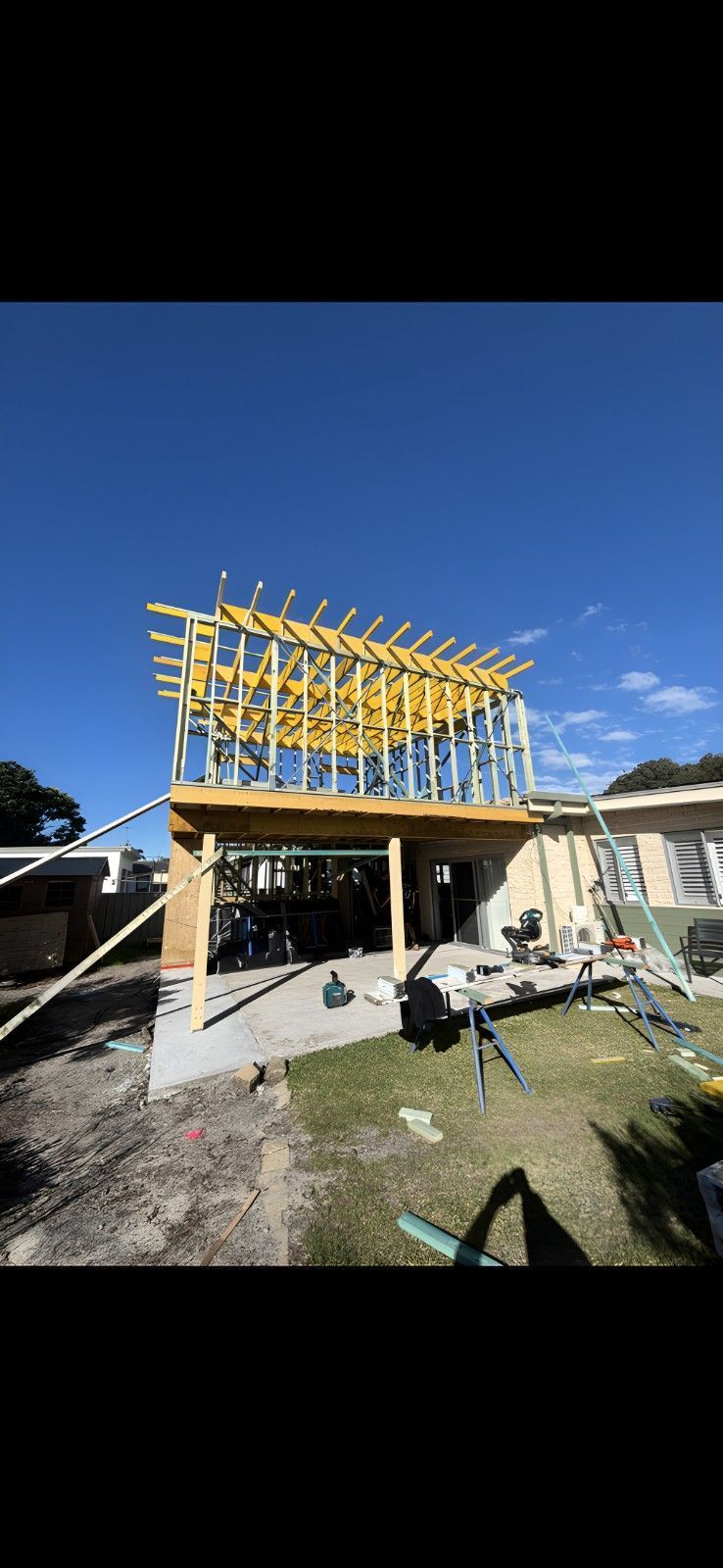 Construction Site of a Two-story Home Extension With Wood Framing Against a Bright Blue Sky. the Ground is Partly Dirt, Partly Grass — Campbell Built in Nelson Bay, NSW