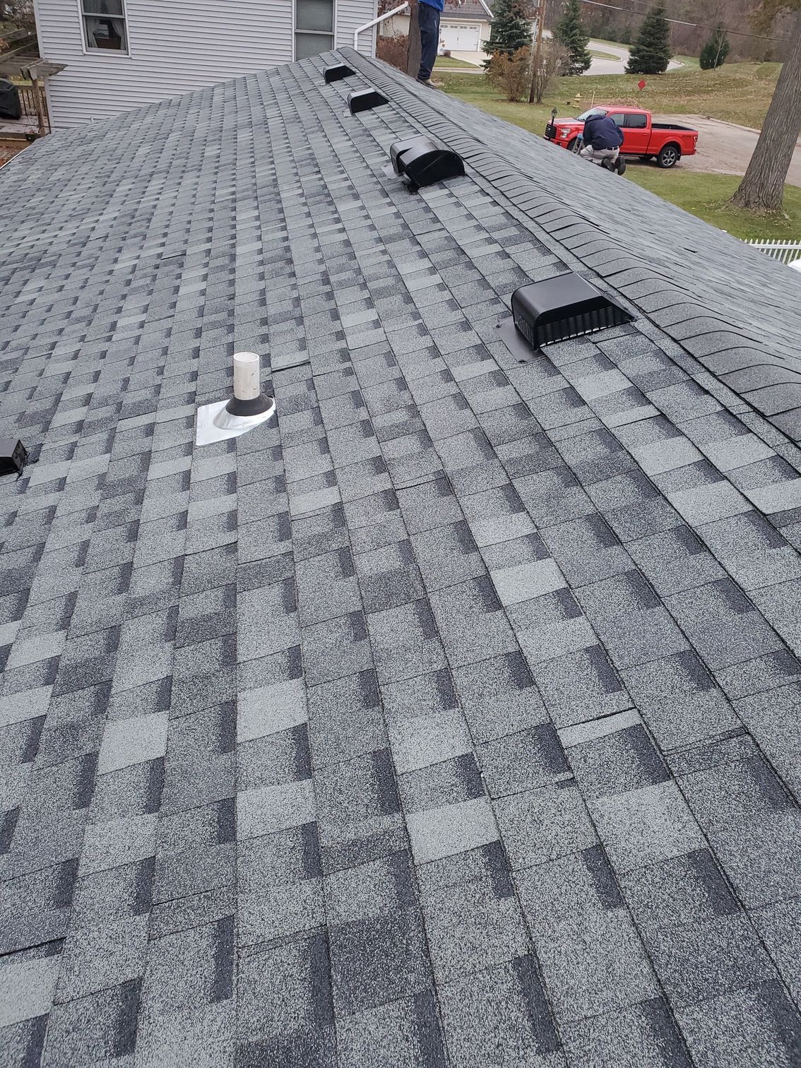 A gray shingle roof with vents. A person stands on the roof near the peak.