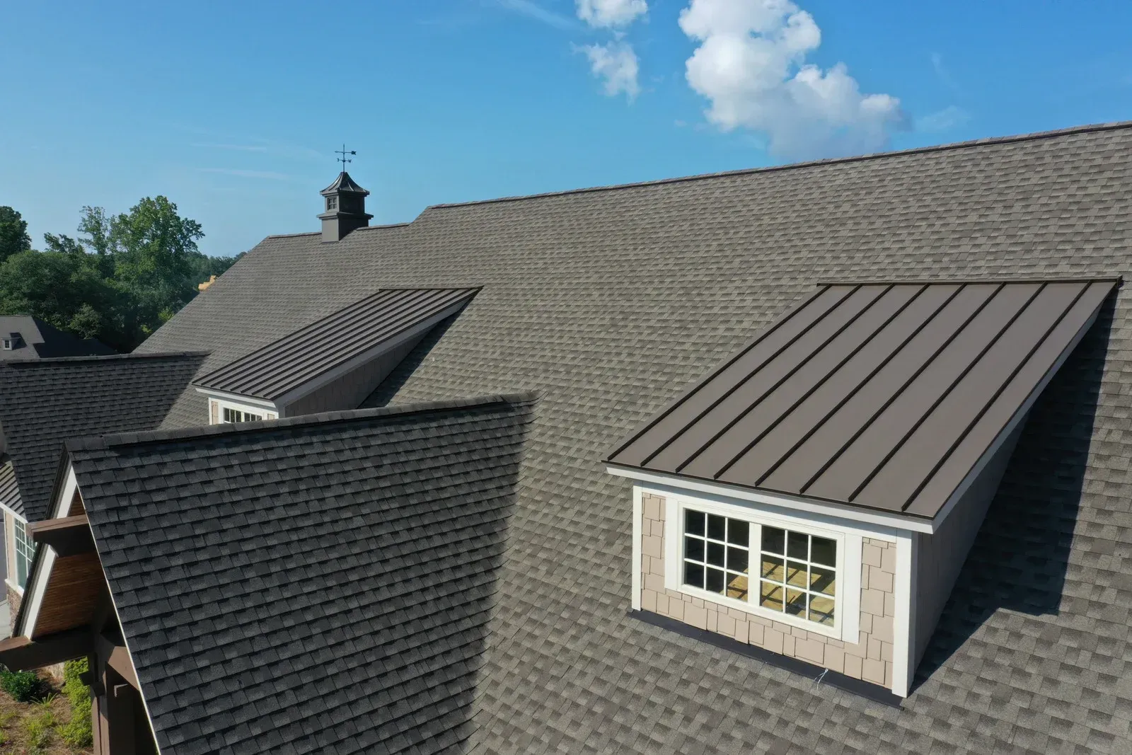 A gray shingled roof with metal dormers against a blue sky. A small steeple is visible.