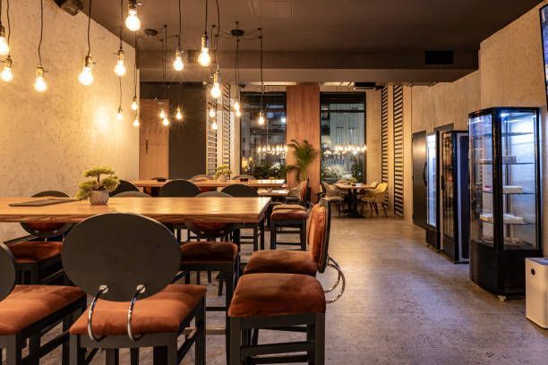 Restaurant interior with wooden tables, orange chairs, and hanging light bulbs.