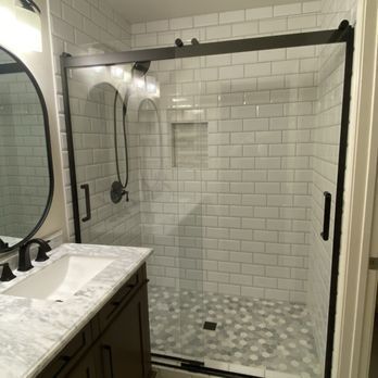 A bathroom vanity with a marble countertop next to a walk-in shower with white subway tiles and black hardware.