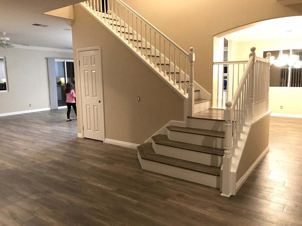 A child stands in an open-plan home interior featuring light wood flooring, beige walls, and a white staircase.