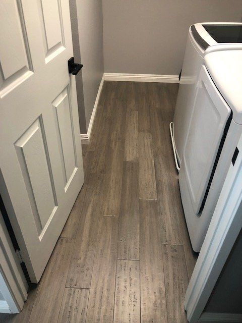 A laundry room with gray wood-look flooring next to a white door and a washing machine.