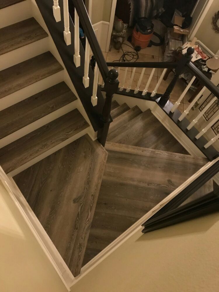 A high-angle view of indoor wooden stairs featuring dark railings and white balusters, with a landing turning the corner.