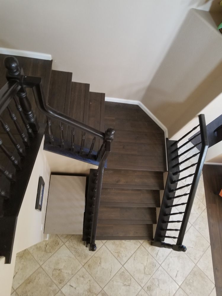 A top-down view of a dark wooden staircase with black railings, leading down to a tiled foyer.