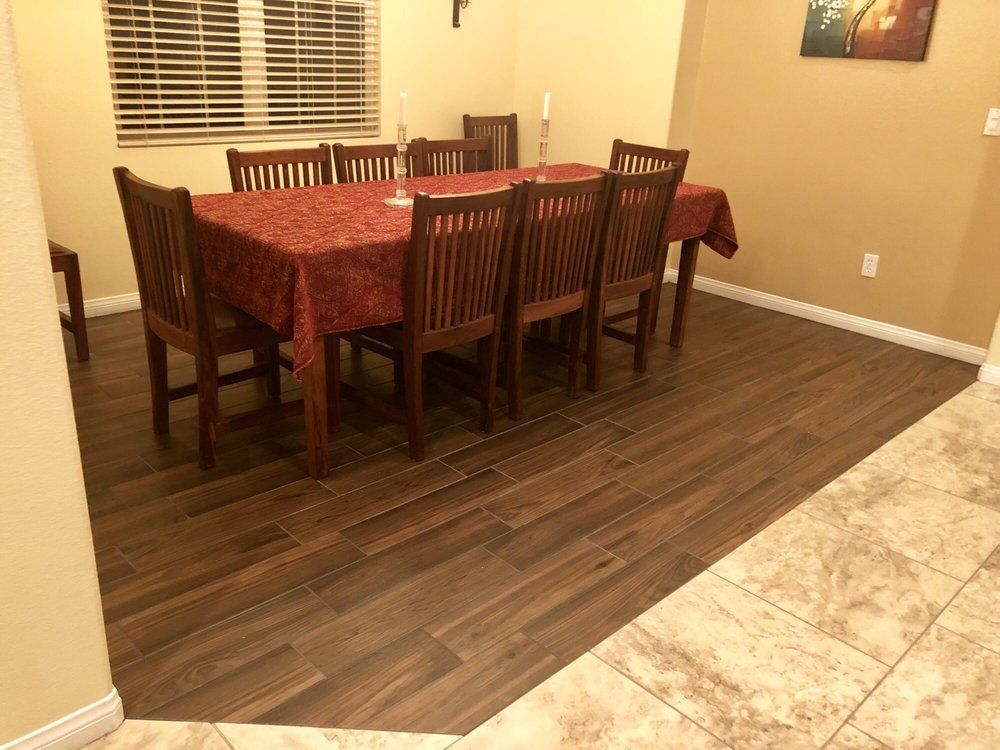 A dining room with a rectangular wooden table and six matching chairs, set on a dark wood floor next to a tiled area.