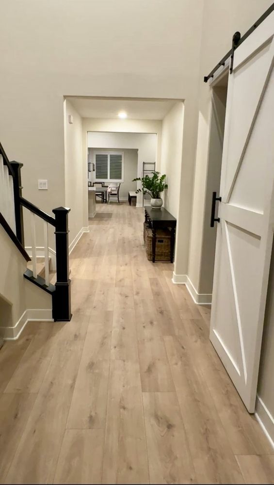 A hallway with light wood flooring, a black-and-white staircase on the left, and a white barn door on the right.