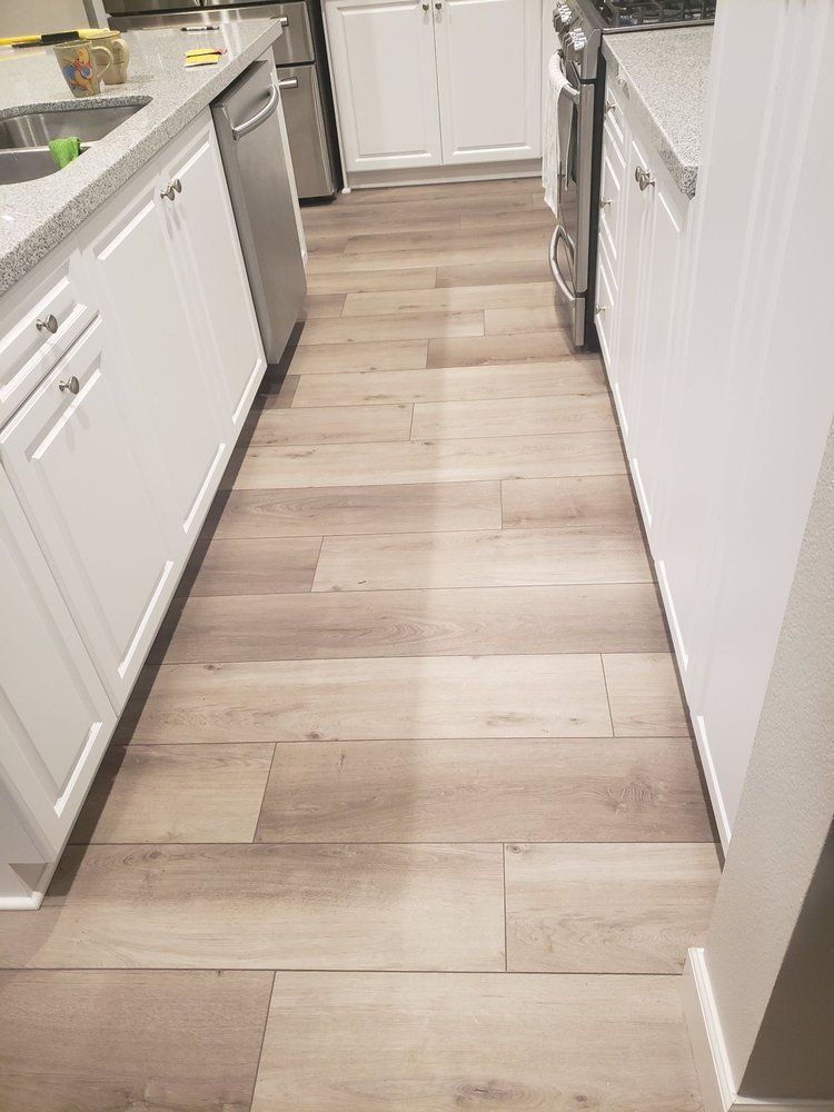 A narrow kitchen galley with light wood-look tile flooring, white cabinets, stainless steel appliances, and quartz counters.