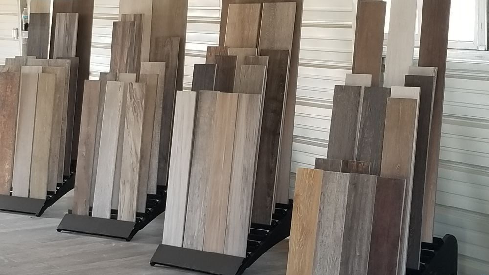 Multiple display racks showcase various wood-look tile planks in shades ranging from light beige to deep brown.