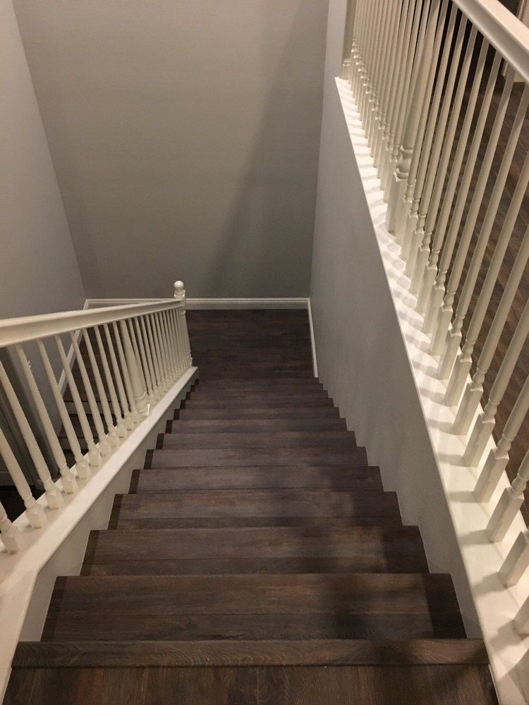 A staircase with dark wood steps and white railings, viewed from the top looking down into a hallway.
