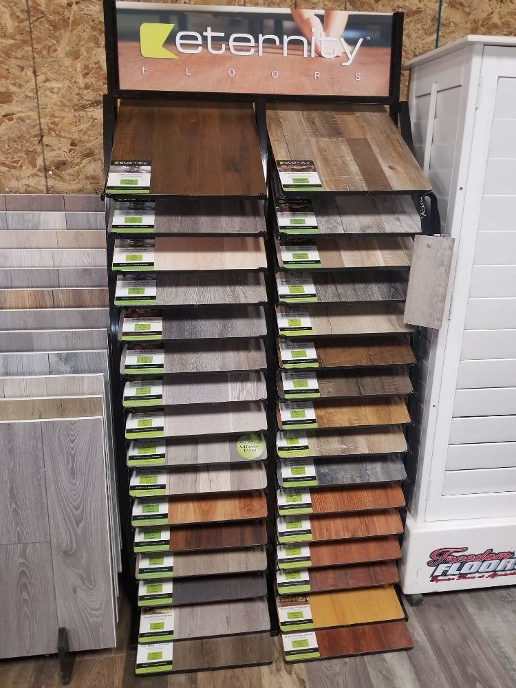 A floor display rack with various wood-look laminate samples, arranged by color and texture, inside a home store.