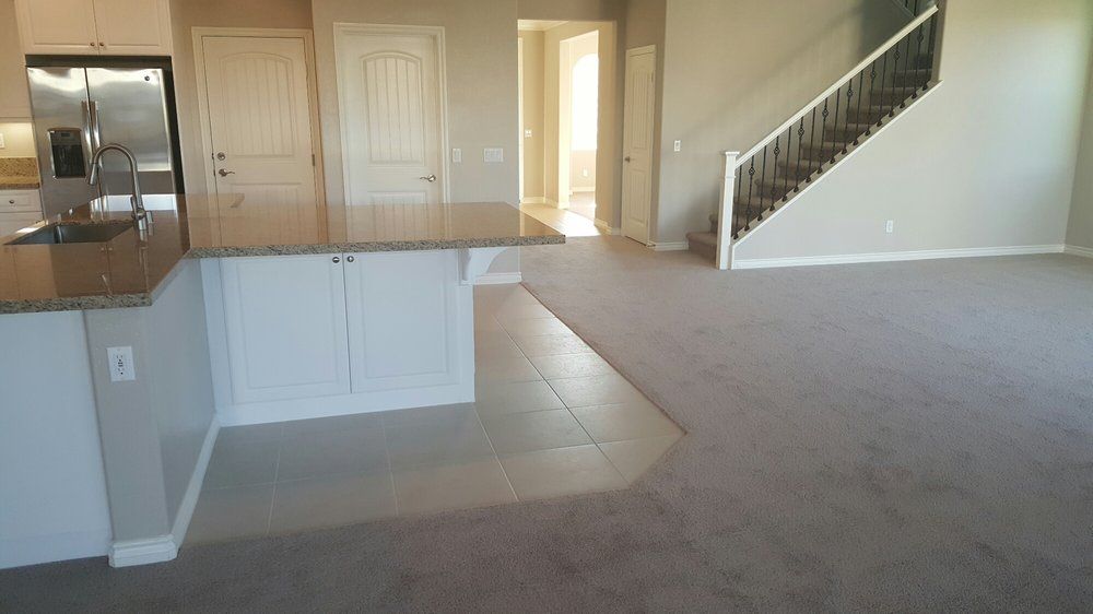 A kitchen island with a granite countertop and white cabinets, situated next to carpeted flooring and a staircase.