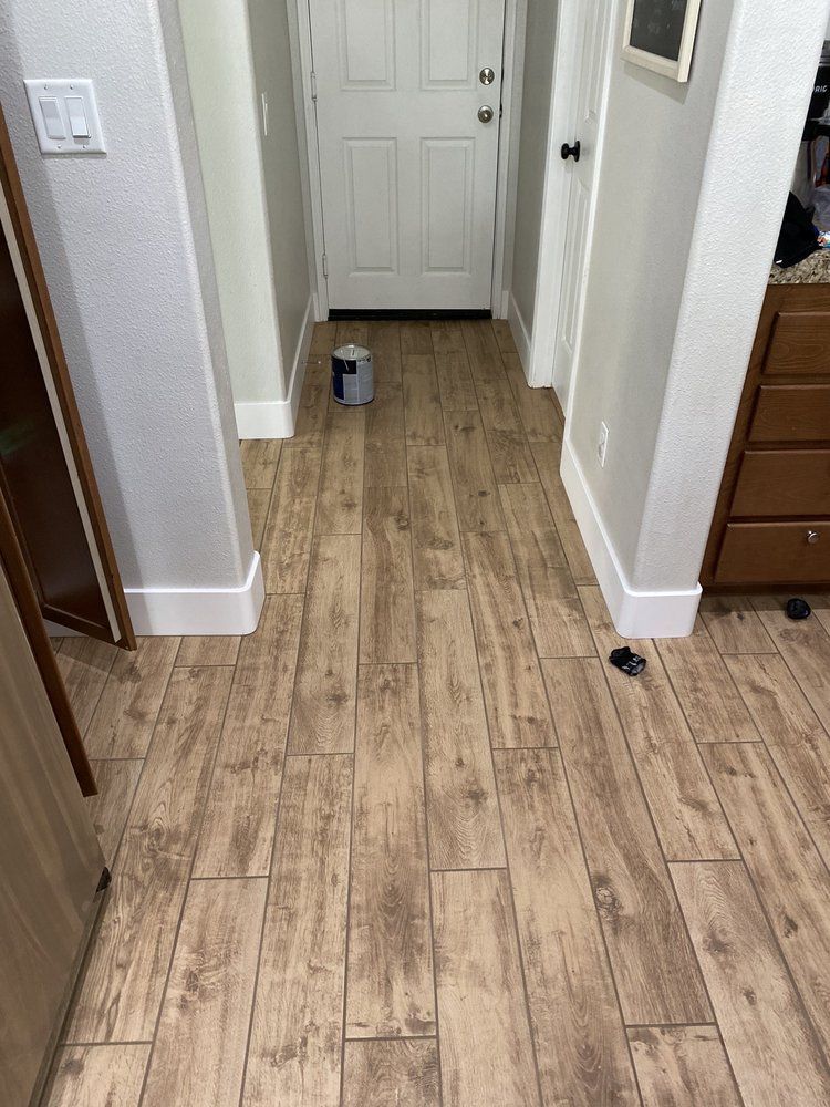 A hallway with wood-look tile flooring, white baseboards, and two doorways, with a paint can sitting on the floor.
