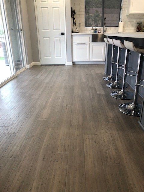 A kitchen with wood-look laminate flooring, white cabinetry, a sink, and three modern bar stools at a dark kitchen island.