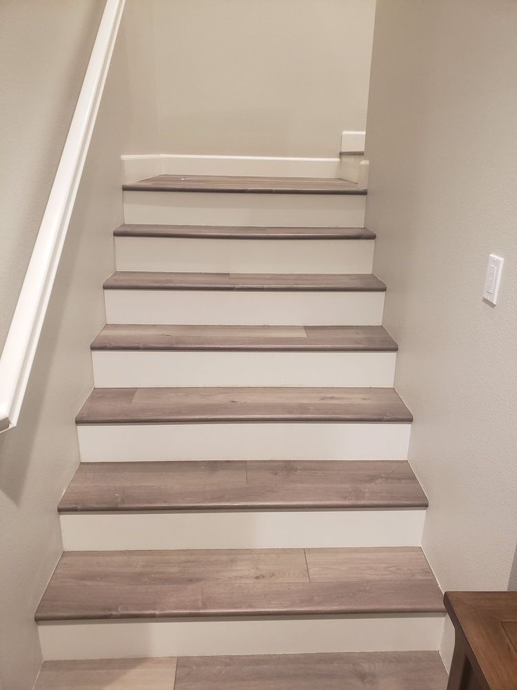 A straight staircase with gray wood-look treads and white risers, viewed from the bottom looking up.
