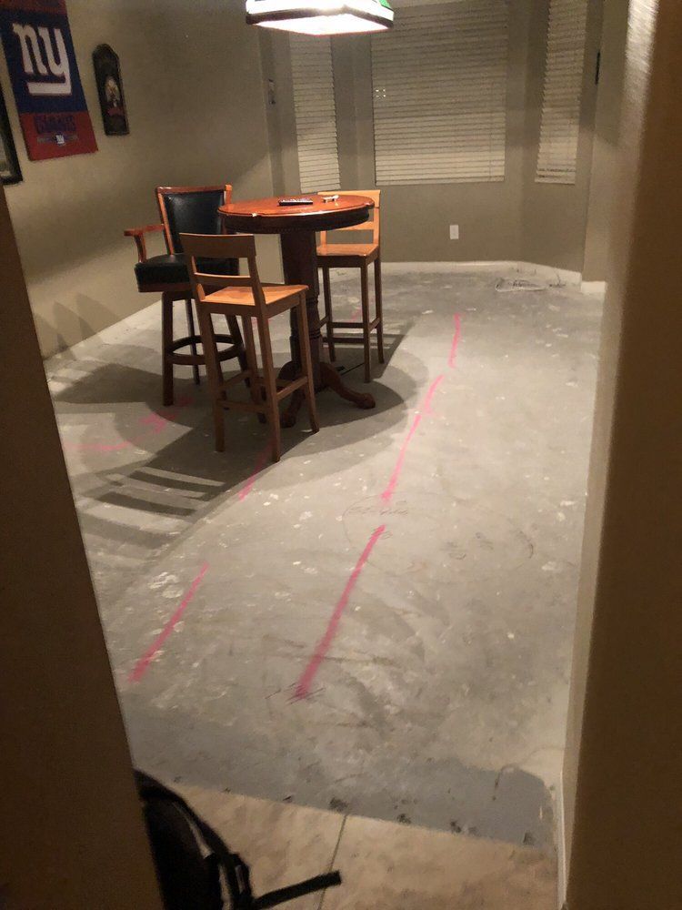 A room with bare concrete floors featuring red chalk lines, a small circular table, and bar stools.