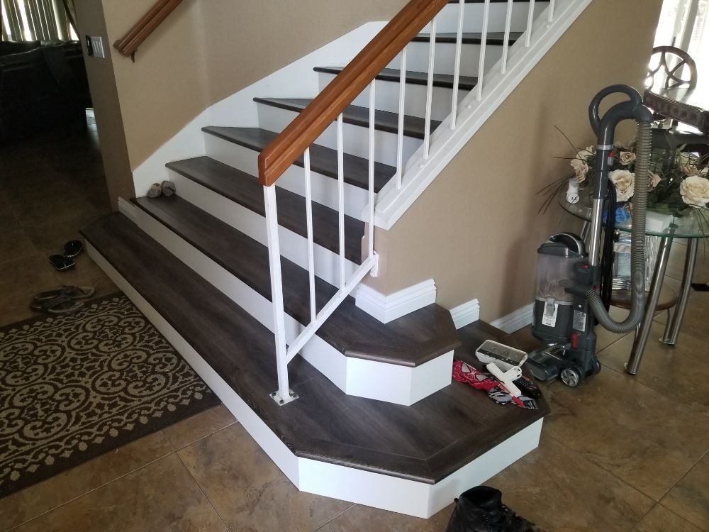 A staircase with dark wood-look steps, white risers, and a white metal railing with a wooden handrail in a home.