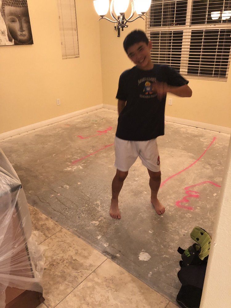 A person posing and smiling in a room under renovation with an exposed concrete floor and pink markings.