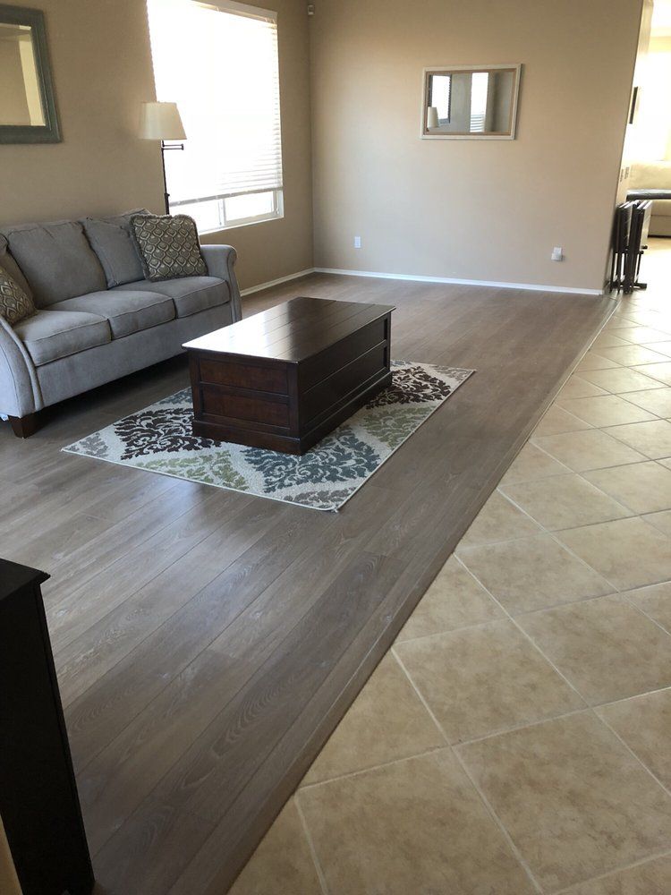 A living room with gray flooring meets beige tile, featuring a gray couch, patterned rug, and a dark wood coffee table.