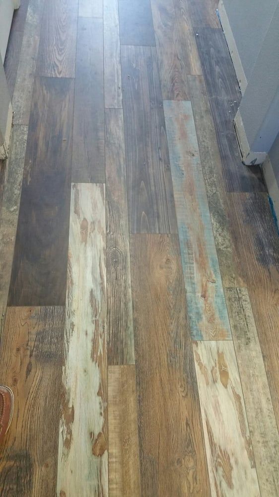 A hallway floor featuring rustic, distressed wood-look vinyl planks with varied brown, gray, and whitewashed tones.