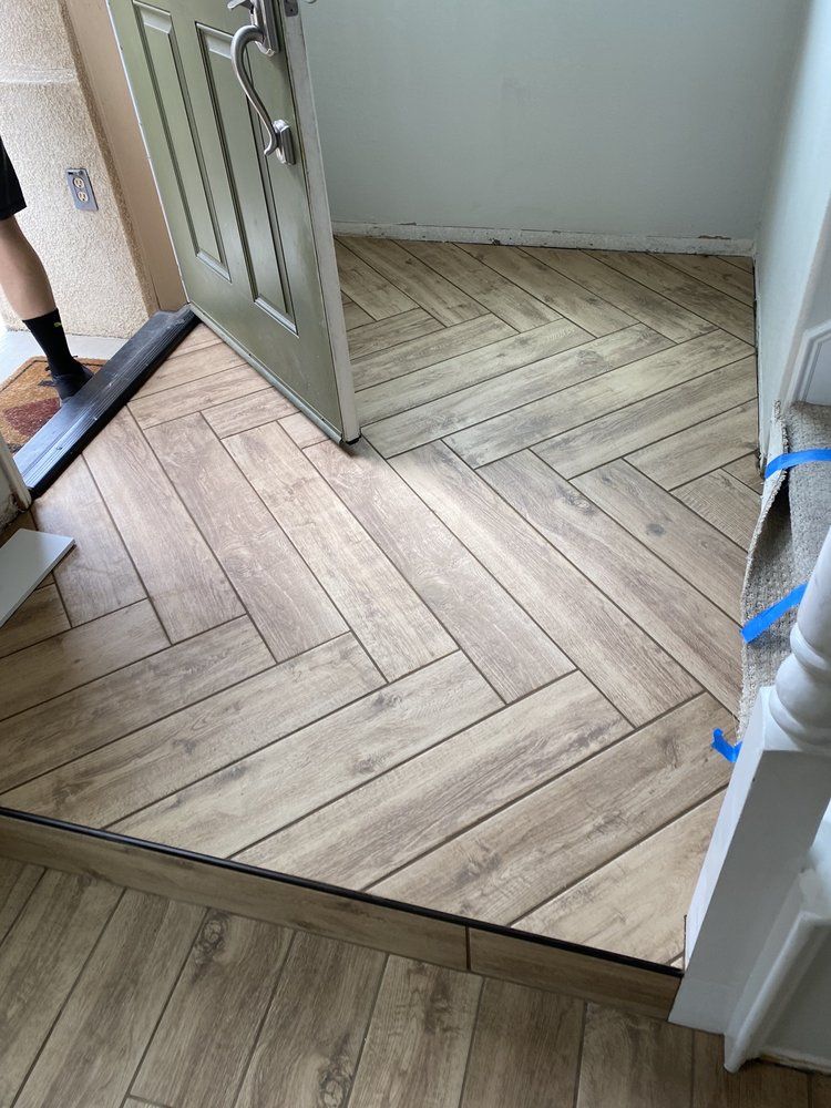 An entryway with wood-look tile flooring laid in a herringbone pattern, featuring a door threshold and a floor transition.