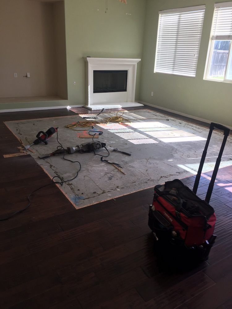 A room with dark wood flooring, a central area under construction, power tools, and a red rolling tool bag.