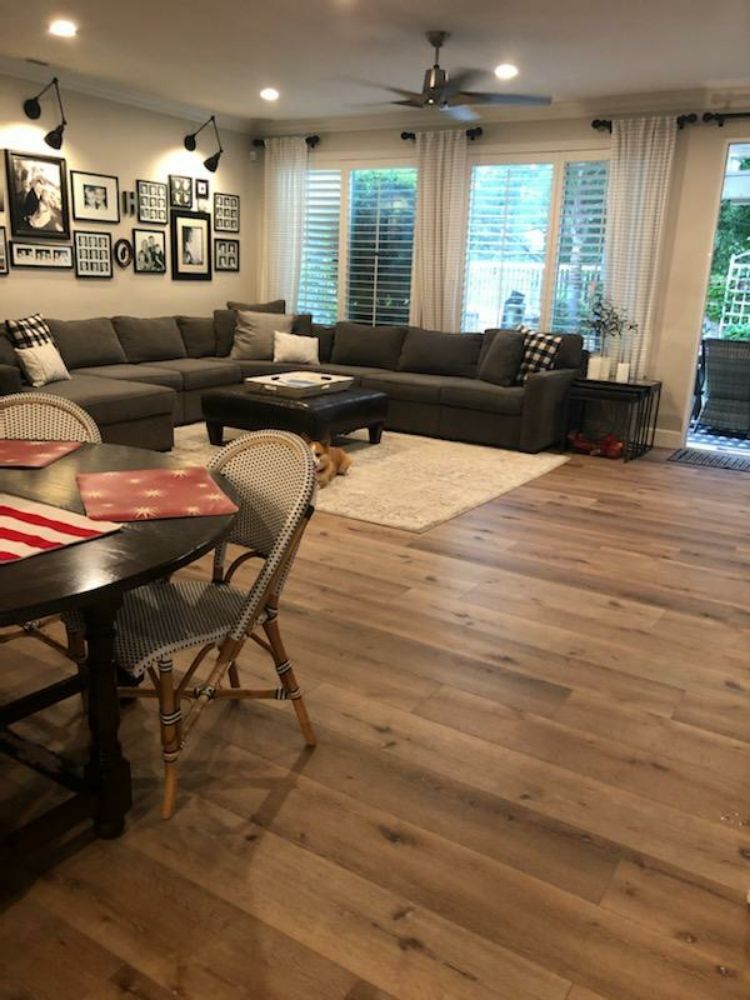 A living room with a large gray sectional sofa, coffee table, and dining set on light hardwood floors under a ceiling fan.