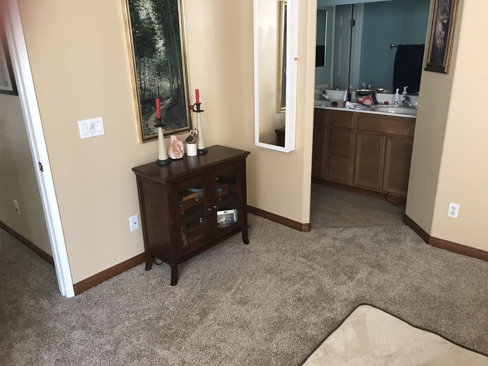 A small dark wood cabinet stands against a tan wall next to an open doorway leading to a bathroom.