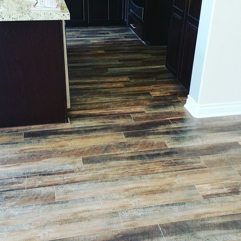 Dark brown wood-look plank flooring in a kitchen next to dark cabinets and a light-colored countertop.