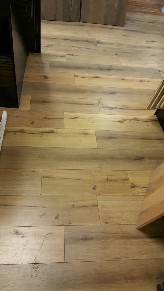 A close-up of light-toned, rustic wood plank flooring with natural grain patterns, knots, and varying brown hues.