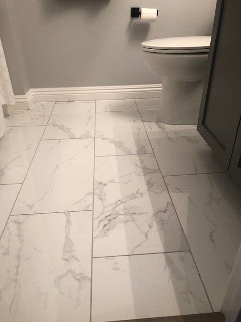 A view of bathroom flooring with white marble-patterned rectangular tiles next to a grey vanity and toilet.