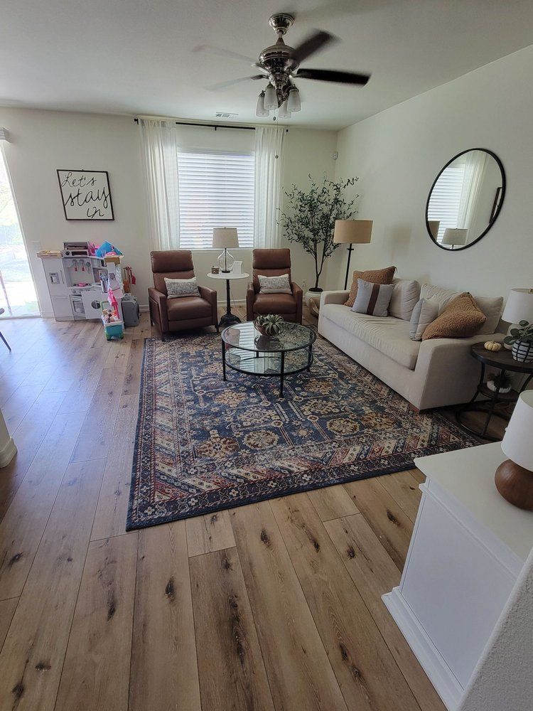 A living room with a cream sofa, two brown leather recliners, a blue patterned rug, and light wood flooring.