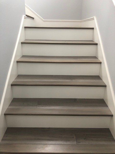 Straight wooden staircase with dark brown treads and white risers against light grey walls.