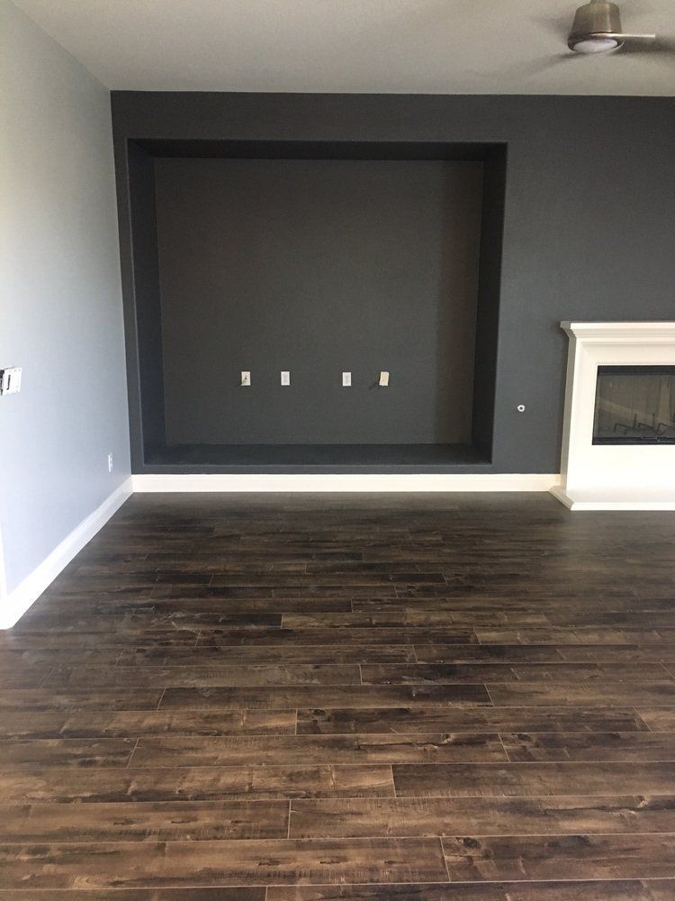 A living room featuring dark wood floors, a charcoal grey accent wall with a recessed TV niche, and a white fireplace.