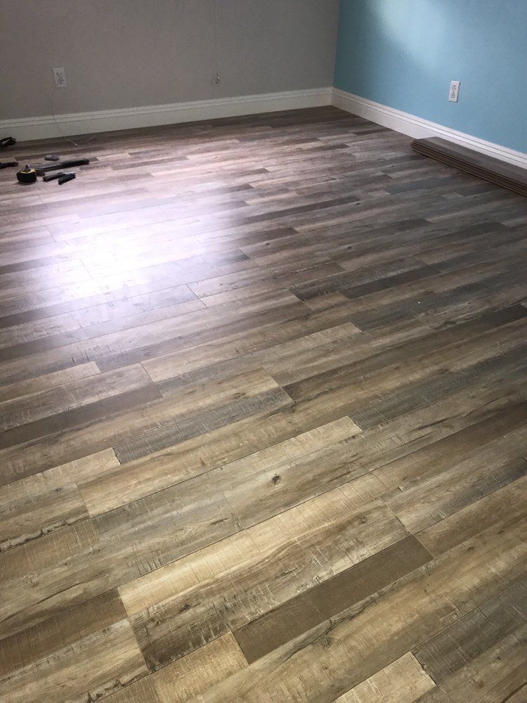 A room with newly installed, wood-look vinyl plank flooring in varying shades of grey and brown, with white baseboards.