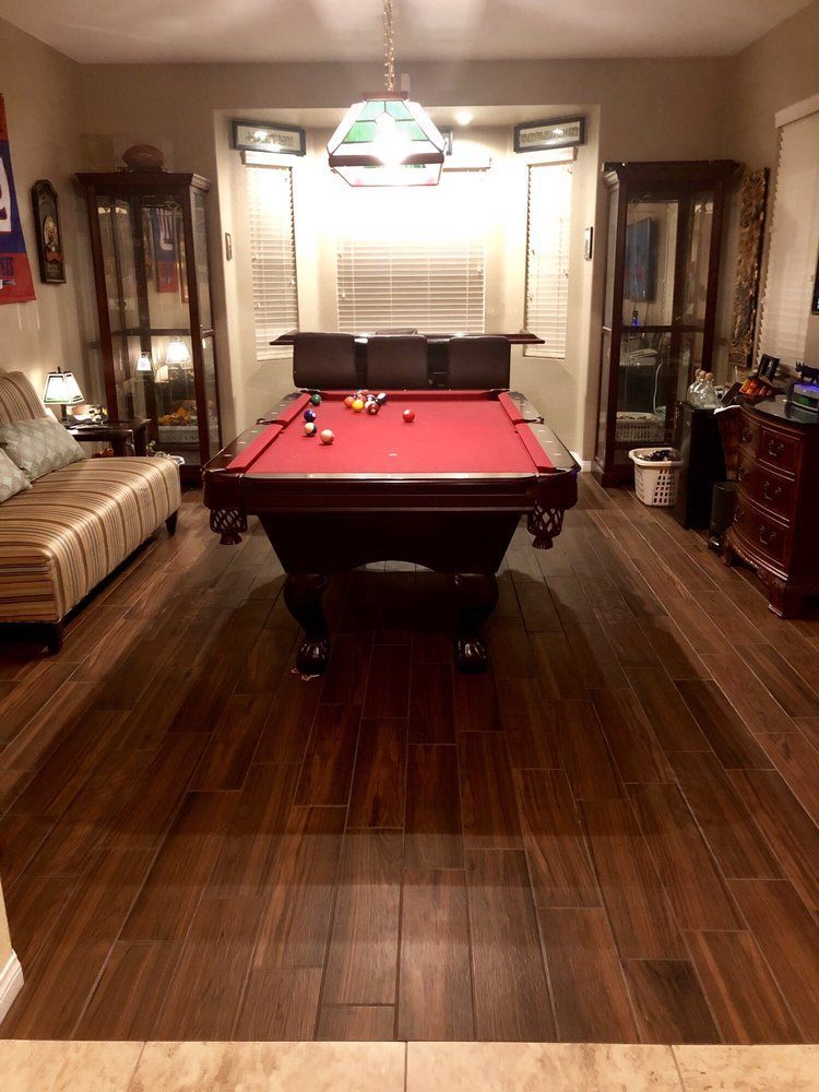 A game room featuring a red felt pool table, a striped sofa, two tall glass display cabinets, and dark wood flooring.