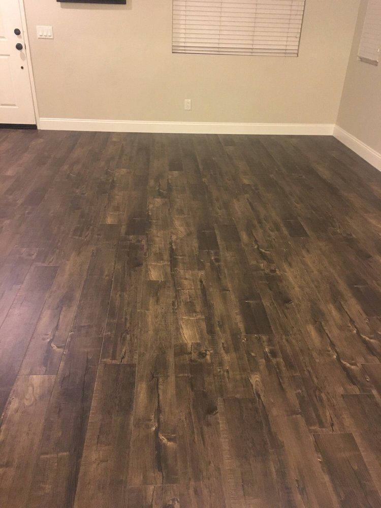 A room with dark brown wood-grain laminate flooring, light beige walls, white baseboards, and a window with blinds.