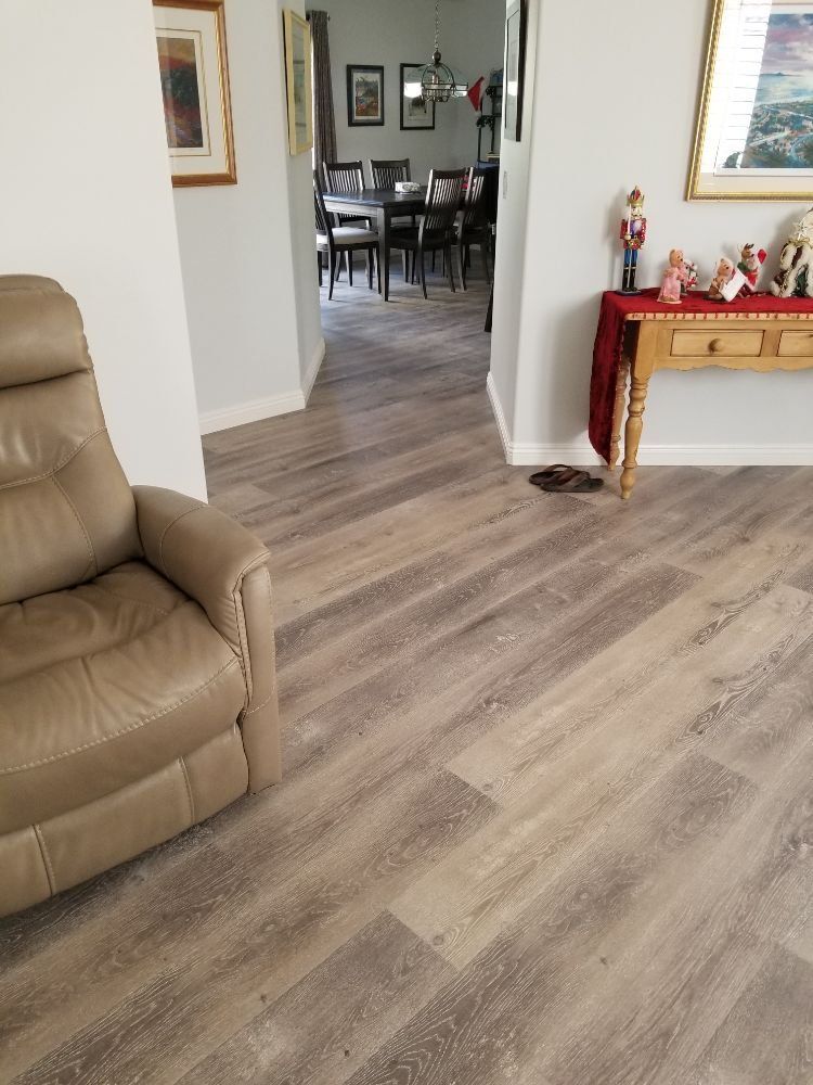 A tan recliner sits in a room with light wood flooring, leading toward a dining area and a console table with decor.