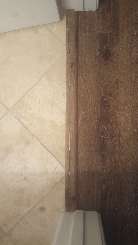 A floor transition featuring a wood-look plank floor meeting diagonal light-colored tiles, separated by a wood threshold.
