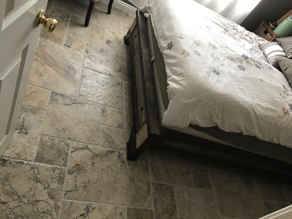 A bedroom with a rustic wooden bed frame on a floor covered in large, multi-sized natural stone tiles.