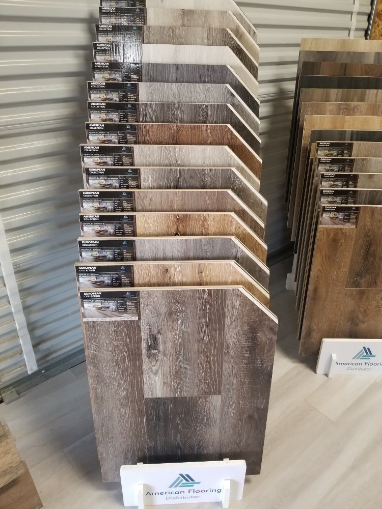 Two display racks hold various wooden-look vinyl flooring samples in a range of brown, gray, and beige wood tones.