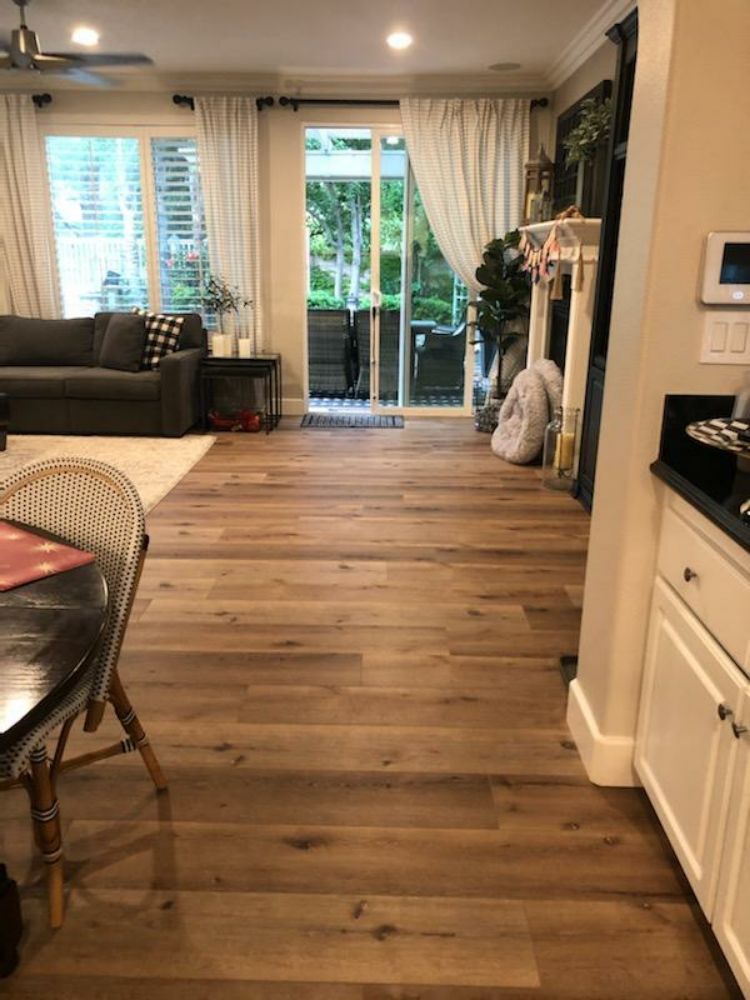 A view looking from a kitchen across light wood flooring toward a living room and sliding glass doors to a patio.