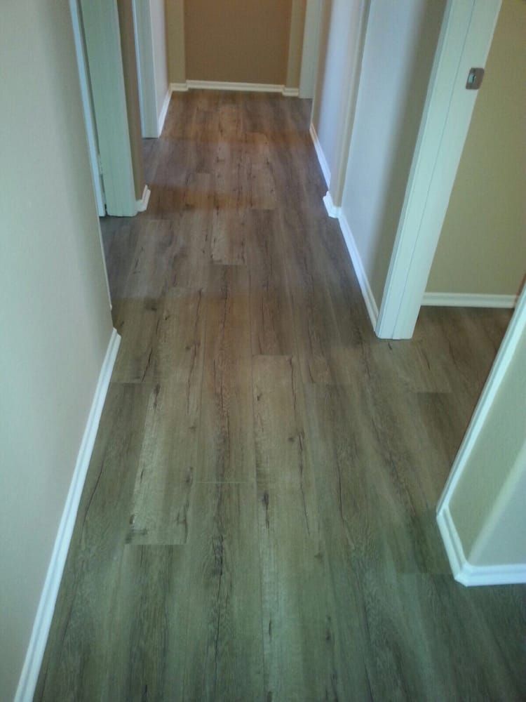 A narrow hallway with brown and grey wood-look plank flooring between light-colored walls and white trim.