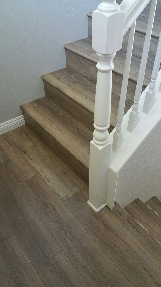 A staircase featuring wood-look vinyl planks, a white wooden railing, and a gray wall.