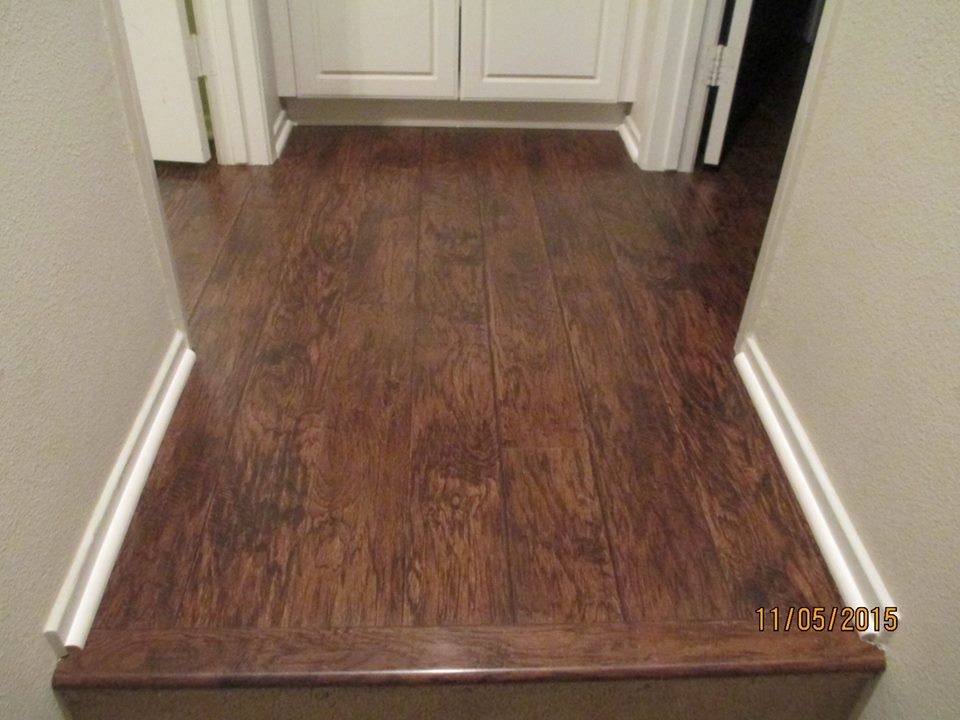 A hallway with dark wood-look laminate flooring leading to a white cabinet, flanked by two walls with white baseboards.