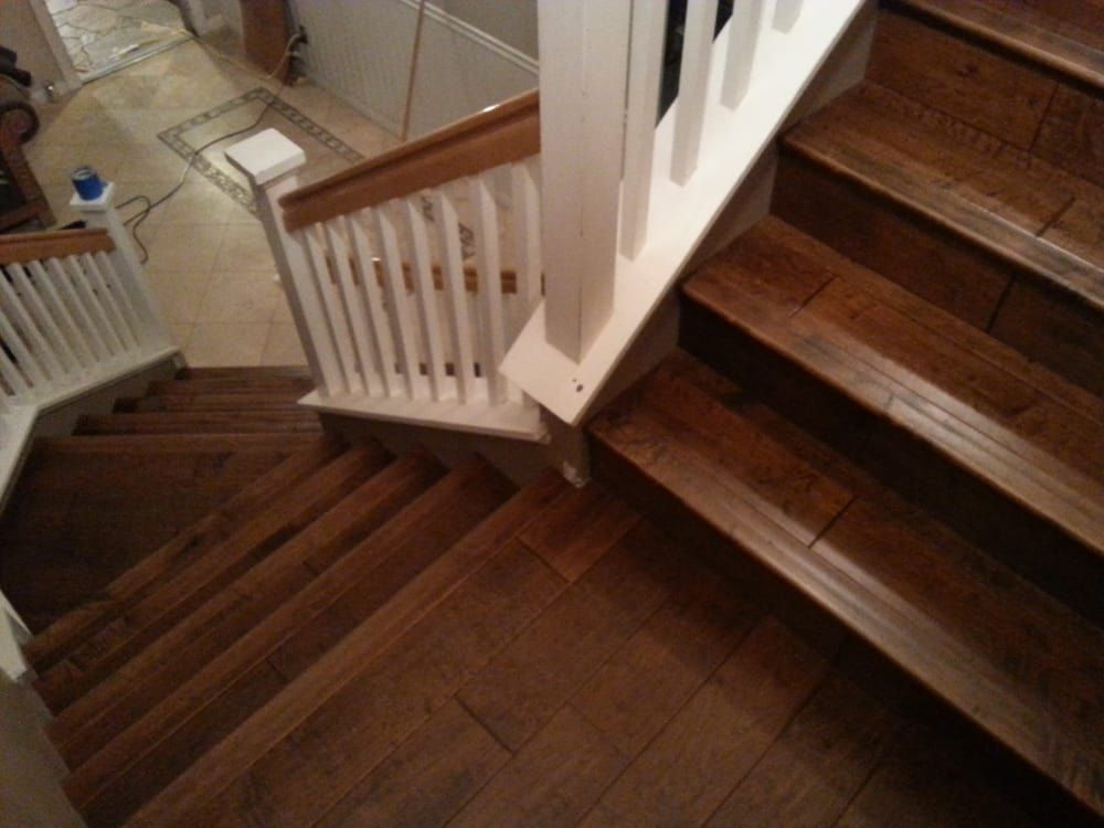 An overhead view of wooden stairs with white railings, descending toward a tiled floor in a home interior.
