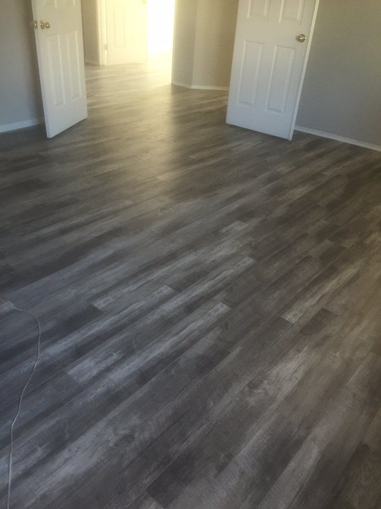 An indoor room with gray wood-look laminate flooring and two open white doors leading to an adjacent lit room.